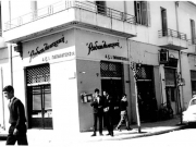 Το κατάστημα «Ραδιοηλεκτρική» των αφών Α. και Ι. Παπαχατζή  και το Ξενοδοχείον «Ελλάς», στη γωνία των οδών Ασκληπιού και Κούμα.  Μεταπολεμική φωτογραφία. Αρχείο Θανάση Μπετχαβέ