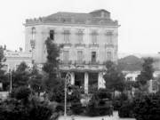Το τριώροφο κτίριο «Πανελλήνιον» της πλατείας Θέμιδος (Κεντρικής), στο ισόγειο του οποίου στεγαζόταν για δέκα και πλέον χρόνια το καφενείο «Ντορέ». Λεπτομέρεια κάρτας του Ιωάν. Κουμουνδούρου. 1932