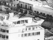 Το κτίριο της Λέσχης Αξιωματικών Φρουράς Λαρίσης και πίσω του η οδός Πανός. Το βέλος υποδεικνύει την δυτική είσοδο της Στοάς Κουτσίνα και πίσω διακρίνεται μέρος από τις στέγες των καταστημάτων της. Αεροφωτογραφία του 1960 περίπου