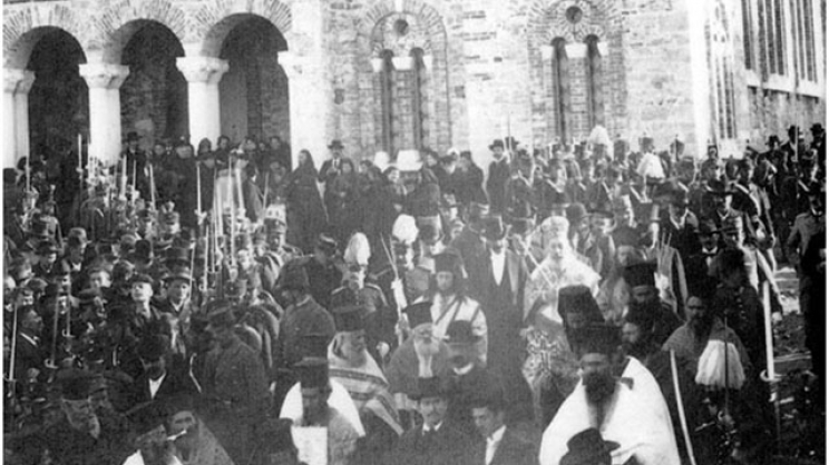 Η πομπή των Θεοφανείων του 1905 στην αυλή του ναού του Αγ. Αχιλλίου, έτοιμη  να κατεβεί τα σκαλοπάτια και να κατευθυνθεί στη γέφυρα του Πηνειού. Λεπτομέρεια  φωτογραφίας του Γεωργίου Λαμπάκη. Αρχείο του Ιωάννη Ρούσκα.