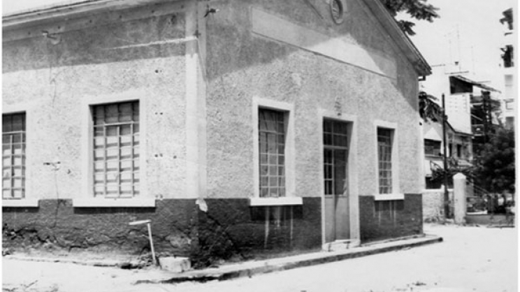 Το κτίριο των ηλεκτρικών εγκαταστάσεων του ΟΥΗΛ, στη θέση όπου σήμερα έχει κατασκευαστεί το ημιτελές Θέατρο του ΟΥΗΛ. Φωτογραφία του 1990. Από το αρχείο του Βαγγέλη Ρηγόπουλου μέλους της Φωτοθήκης Λάρισας.