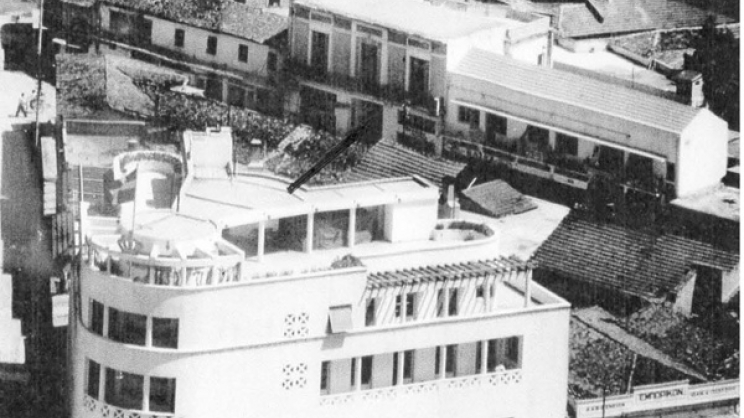 Το κτίριο της Λέσχης Αξιωματικών Φρουράς Λαρίσης και πίσω του η οδός Πανός. Το βέλος υποδεικνύει την δυτική είσοδο της Στοάς Κουτσίνα και πίσω διακρίνεται μέρος από τις στέγες των καταστημάτων της. Αεροφωτογραφία του 1960 περίπου