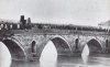 Τα τρία μεσαία τόξα της παλιάς πέτρινης γέφυρας του Πηνειού σε μια φωτογραφία των χρόνων της τουρκοκρατίας (1878;). Φωτογραφία άγνωστου, παρμένη κατά τη διάρκεια της εορτής των Θεοφανείων. Από το βιβλίο &quot;Λάρισα. Εικόνες του χθες&quot; με φωτογραφίες του Τάκη Τλούπα και κείμενα του Νίκου Νάκου, (1986) σελ. 46